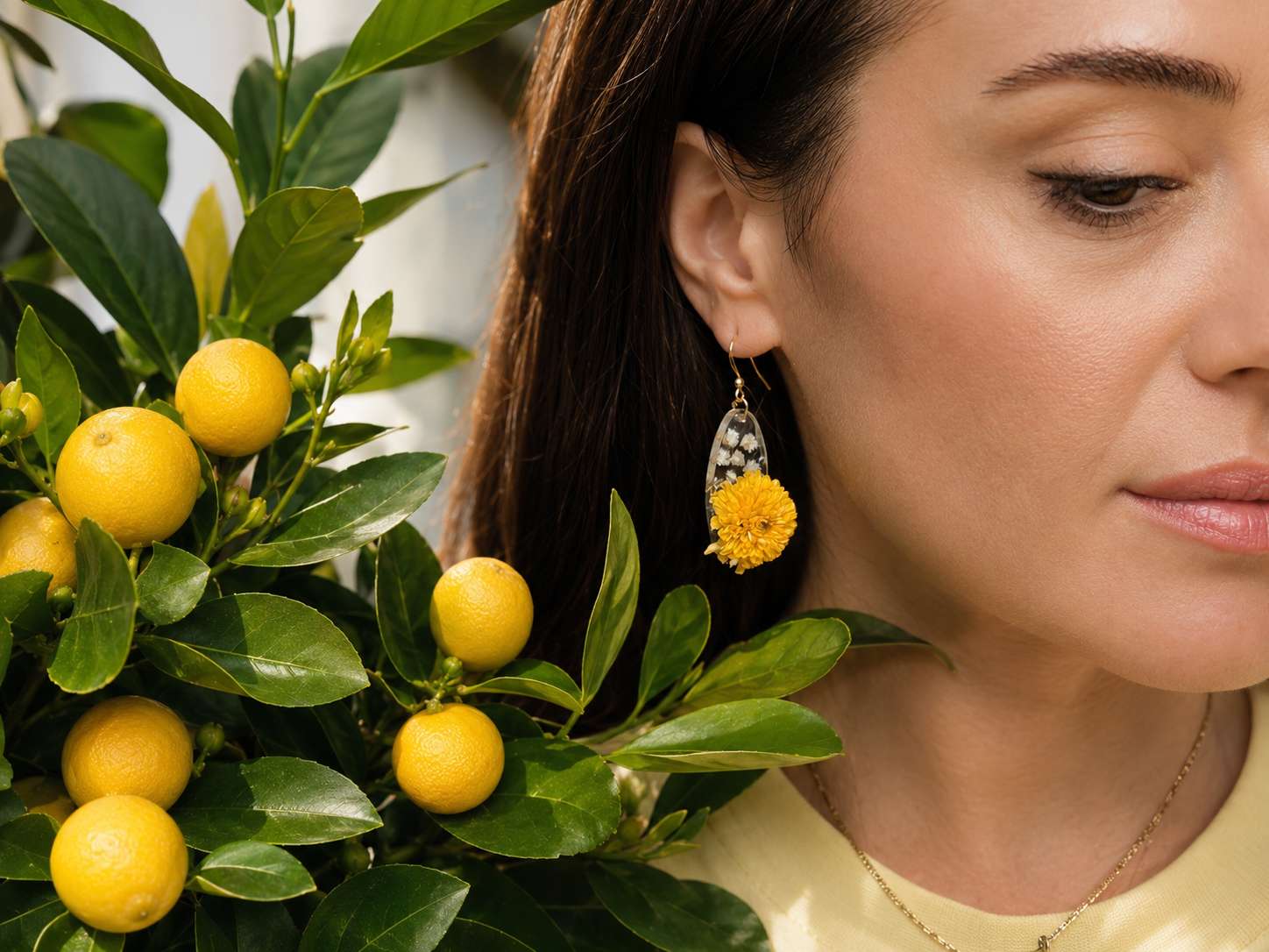 Frau trägt handgefertigten Ohrhänger von Laia Studios mit gelber Chrysantheme in kristallklarem Harz, neben einem Zitronenbaum